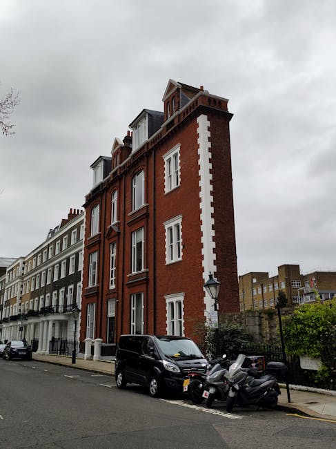 A series of white painted columns and walls forming a covered corridor or walkway outside a property, with black wrought iron fences and fencing along the edge. Potted plants with flowers are placed o