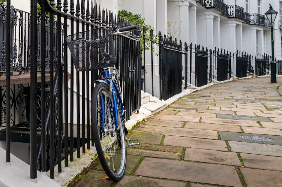 Photograph of a narrow street in Earls Court with limited vehicle access due to an historic brick archway connecting two buildings, one on each side of the alley. The archway features detailed brickwo